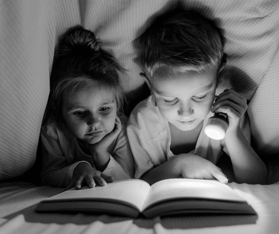 ילדים קוראים לאור פנס מתחת לשמיכה
